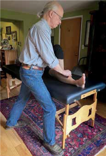 a man performs bodywork on the lower legs of a person lying on a massage table